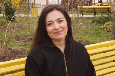 Natasha is sitting on a park bench, smiling into the camera.